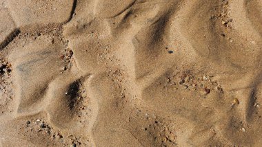 Kumsal kum dokusu. Geniş, dalgalı, kısa yatay çizgiler, dalgalanmalar ve rüzgarın oluşturduğu desenlerle dokulu bir kum yüzeyinin yakın çekimi. Renkler ışıktan koyu kahverengiye değişir.