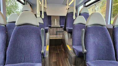 Boş mavi koltukları ve gri başlıkları olan temiz ve modern bir şehir otobüsü manzarası. Geniş pencereler doğal gün ışığını içeri alarak sakin ve rahat bir atmosfer yaratıyor. Toplu taşıma, kentsel seyahat ve günlük seyahat kavramı.