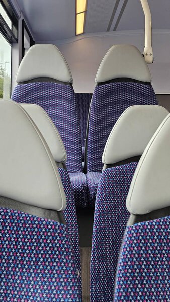 Вид на чистый и современный интерьер городского автобуса с пустыми синими сиденьями и подголовниками. Большие окна впускают естественный дневной свет, создавая спокойную и комфортную атмосферу. Общественный транспорт, городские поездки и ежедневные поездки на работу и обратно.