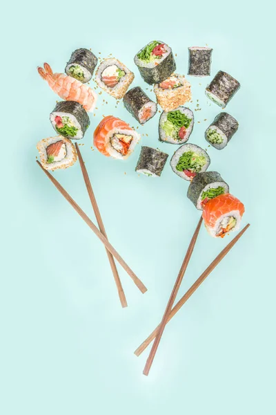 箸で空飛ぶ寿司 薄青を基調とした様々なおいしい日本の寿司 ロールピース — ストック写真