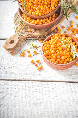  Küçük organik ahşap kasede deniz dikenli üzümler, beyaz ahşap masa arka planında deniz dikenli dallar