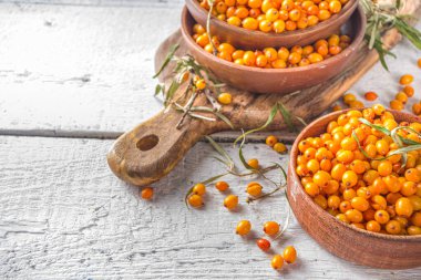  Küçük organik ahşap kasede deniz dikenli üzümler, beyaz ahşap masa arka planında deniz dikenli dallar