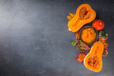 Sonbahar geleneksel pişirme arka planı. Balkabağı turtası, balkabağı baharatı, yarım dilimlenmiş balkabağı, un, kap kacak ve sonbahar dekorasyonu için malzemeler, üst görünüm kopya alanı