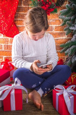 Noel ağacıyla evde akıllı telefonu olan küçük tatlı kız hediye kutuları ve Xmas dekoru sunar, Covid-19, karantina geçmişinde Noel 'i kutluyor. 