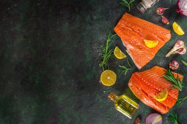 Somon balığı. Taze çiğ somon balığı filetosu. Pişirme malzemeleri, otlar ve limon dilimleme tahtasında, siyah yeşil arka plan, üst görünüm. 
