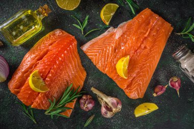 Somon balığı. Taze çiğ somon balığı filetosu. Pişirme malzemeleri, otlar ve limon dilimleme tahtasında, siyah yeşil arka plan, üst görünüm. 