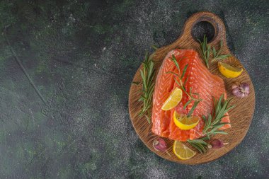 Somon balığı. Taze çiğ somon balığı filetosu. Pişirme malzemeleri, otlar ve limon dilimleme tahtasında, siyah yeşil arka plan, üst görünüm. 