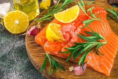 Somon balığı. Taze çiğ somon balığı filetosu. Pişirme malzemeleri, otlar ve limon dilimleme tahtasında, siyah yeşil arka plan, üst görünüm. 