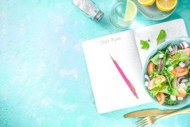 Bir kase sağlıklı sebze salatası, domates, peynir, soğan, zeytin yağı, açık mavi beton arka plan ve diyet planı için not defteri kopyalama alanı.