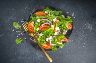 Bir kase sağlıklı sebze salatası, domates, peynir, soğan, zeytin yağı, koyu gri arka plan fotokopi alanı.