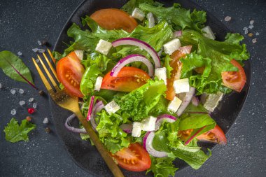 Bir kase sağlıklı sebze salatası, domates, peynir, soğan, zeytin yağı, koyu gri arka plan fotokopi alanı.