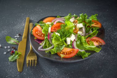 Bir kase sağlıklı sebze salatası, domates, peynir, soğan, zeytin yağı, koyu gri arka plan fotokopi alanı.