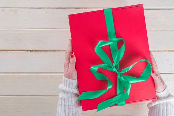 女人手中的大圣诞礼物 大红色圣诞礼品盒 绿带喜庆 女孩子们手拿着照片 顶部是木制背景 — 图库照片