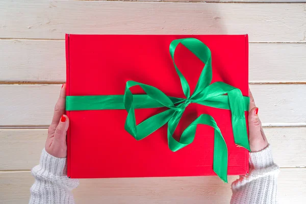 女人手中的大圣诞礼物 大红色圣诞礼品盒 绿带喜庆 女孩子们手拿着照片 顶部是木制背景 — 图库照片