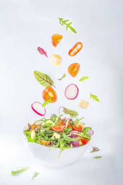 Taze renkli bahar salatası. Avokado, domates, marul, soğan, turp, salatalık, peynir. Beyaz kasede beyaz arka planda fotokopi alanı, havada asılı malzemelerle. 