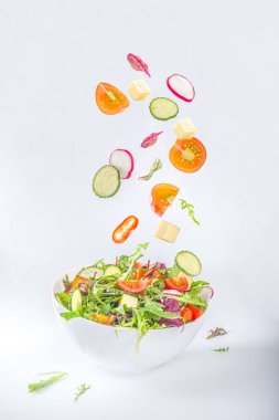 Taze renkli bahar salatası. Avokado, domates, marul, soğan, turp, salatalık, peynir. Beyaz kasede beyaz arka planda fotokopi alanı, havada asılı malzemelerle. 