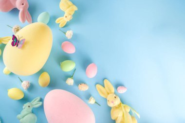 Paskalya Bayramı tebrik kartı, indirim, davetiye geçmişi. Renkli Paskalya Yumurtaları ve Tavşancıklar, mavi arkaplan üzerinde bahar çiçekleri metin alanı için fotokopi alanı ile üst görünüm düz
