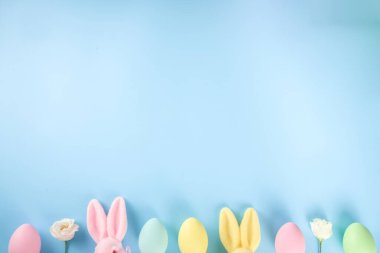 Paskalya Bayramı tebrik kartı, indirim, davetiye geçmişi. Renkli Paskalya Yumurtaları ve Tavşancıklar, mavi arkaplan üzerinde bahar çiçekleri metin alanı için fotokopi alanı ile üst görünüm düz