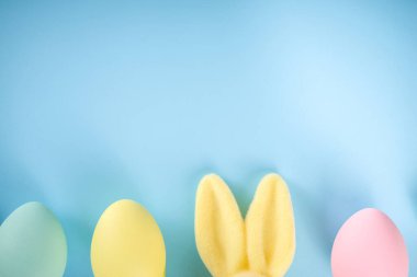 Paskalya Bayramı tebrik kartı, indirim, davetiye geçmişi. Renkli Paskalya Yumurtaları ve Tavşancıklar, mavi arkaplan üzerinde bahar çiçekleri metin alanı için fotokopi alanı ile üst görünüm düz