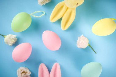 Paskalya Bayramı tebrik kartı, indirim, davetiye geçmişi. Renkli Paskalya Yumurtaları ve Tavşancıklar, mavi arkaplan üzerinde bahar çiçekleri metin alanı için fotokopi alanı ile üst görünüm düz