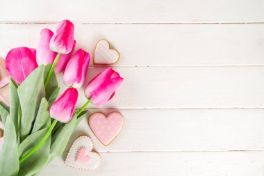 Sevgililer Günü konsepti, Bahar Kadınları Günü Tatili, Anneler Günü arkaplanı, Kırmızı lale çiçeği buketi, el işi kağıt hediye kutusu, kalp şeklinde geleneksel şeker kurabiyeleri, beyaz ahşap arka plan kopyalama alanı.