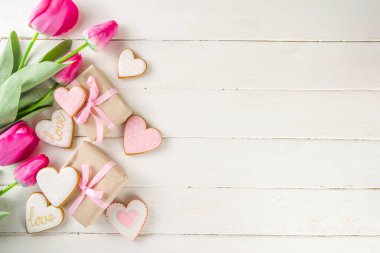 Sevgililer Günü konsepti, Bahar Kadınları Günü Tatili, Anneler Günü arkaplanı, Kırmızı lale çiçeği buketi, el işi kağıt hediye kutusu, kalp şeklinde geleneksel şeker kurabiyeleri, beyaz ahşap arka plan kopyalama alanı.
