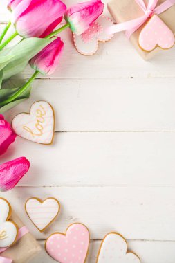 Sevgililer Günü konsepti, Bahar Kadınları Günü Tatili, Anneler Günü arkaplanı, Kırmızı lale çiçeği buketi, el işi kağıt hediye kutusu, kalp şeklinde geleneksel şeker kurabiyeleri, beyaz ahşap arka plan kopyalama alanı.