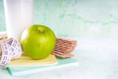  Sağlıklı yemek ve kilo kaybı konsepti. Elma, yoğurt, sağlıklı mısır gevreği, not defteri ve metin için açık yeşil arkaplan fotokopi alanı ölçüm bandı