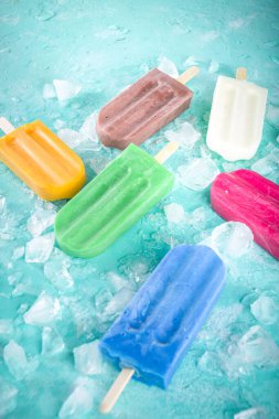 Çok renkli, parlak dondurmalı buzlu dondurma seçimi. Çeşitli dondurmalar, dondurulmuş lolipoplar. Çikolatalı, vanilyalı, böğürtlenli, fıstıklı, portakallı, açık mavi, güneşli arka planda ezilmiş buzlu.