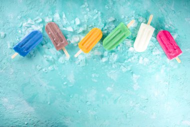 Çok renkli, parlak dondurmalı buzlu dondurma seçimi. Çeşitli dondurmalar, dondurulmuş lolipoplar. Çikolatalı, vanilyalı, böğürtlenli, fıstıklı, portakallı, açık mavi, güneşli arka planda ezilmiş buzlu.