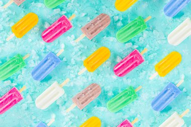 Çok renkli, parlak dondurmalı buzlu dondurma seçimi. Çeşitli dondurmalar, dondurulmuş lolipoplar. Çikolatalı, vanilyalı, böğürtlenli, fıstıklı, portakallı, açık mavi, güneşli arka planda ezilmiş buzlu.