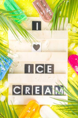Çok renkli, parlak dondurmalı buzlu dondurma seçimi. Çeşitli dondurma, dondurulmuş lolipoplar. Çikolatalı, vanilyalı, böğürtlenli, fıstıklı, portakallı, trend sarı, güneşli arka planda ezilmiş buzlu.