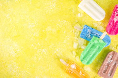 Çok renkli, parlak dondurmalı buzlu dondurma seçimi. Çeşitli dondurma, dondurulmuş lolipoplar. Çikolatalı, vanilyalı, böğürtlenli, fıstıklı, portakallı, trend sarı, güneşli arka planda ezilmiş buzlu.