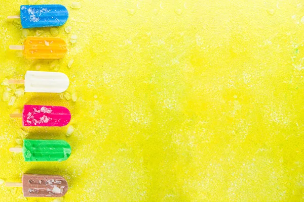 Çok renkli, parlak dondurmalı buzlu dondurma seçimi. Çeşitli dondurma, dondurulmuş lolipoplar. Çikolatalı, vanilyalı, böğürtlenli, fıstıklı, portakallı, trend sarı, güneşli arka planda ezilmiş buzlu.