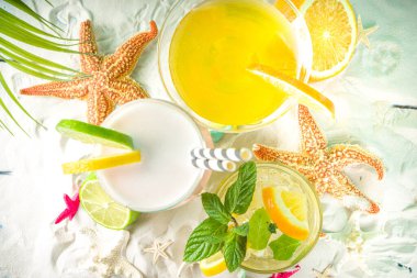 Yaz tropik deniz tatili konsepti. Deniz kabukları ve deniz yıldızlarıyla kumsalda, açık mavi ahşap arka planda, yaz aylarında soğuk kokteyl içecekleri bulunan üç farklı bardak. 