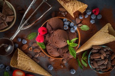 Kara Çikolatalı Dondurma. Bol çikolatalı dondurma, barut ve parçalarla, dondurmalı waffle konileri ve yaz taze meyveleri koyu beton arka plan manzaralı.