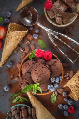Kara Çikolatalı Dondurma. Bol çikolatalı dondurma, barut ve parçalarla, dondurmalı waffle konileri ve yaz taze meyveleri koyu beton arka plan manzaralı.