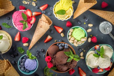 Farklı kaselerde çeşitli renkli dondurma topları, dondurma külahları ve aromalı malzemeler - şam fıstığı, böğürtlen, limon, çikolata, vanilya fasulyesi, nane. Koyu arkaplan kopyalama alanı