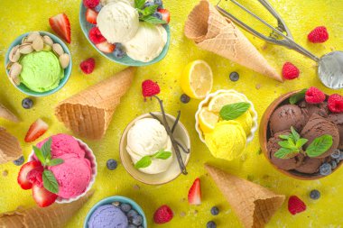 Farklı kaselerde çeşitli renkli dondurma topları, dondurma külahları ve aromalı malzemeler - şam fıstığı, böğürtlen, limon, çikolata, vanilya, nane. Renkli sarı parlak arkaplan
