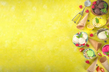 Farklı kaselerde çeşitli renkli dondurma topları, dondurma külahları ve aromalı malzemeler - şam fıstığı, böğürtlen, limon, çikolata, vanilya, nane. Renkli sarı parlak arkaplan