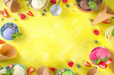 Farklı kaselerde çeşitli renkli dondurma topları, dondurma külahları ve aromalı malzemeler - şam fıstığı, böğürtlen, limon, çikolata, vanilya, nane. Renkli sarı parlak arkaplan