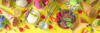 Farklı kaselerde çeşitli renkli dondurma topları, dondurma külahları ve aromalı malzemeler - şam fıstığı, böğürtlen, limon, çikolata, vanilya, nane. Renkli sarı parlak arkaplan