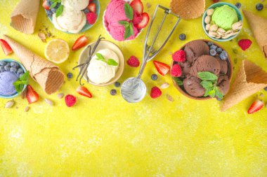 Farklı kaselerde çeşitli renkli dondurma topları, dondurma külahları ve aromalı malzemeler - şam fıstığı, böğürtlen, limon, çikolata, vanilya, nane. Renkli sarı parlak arkaplan