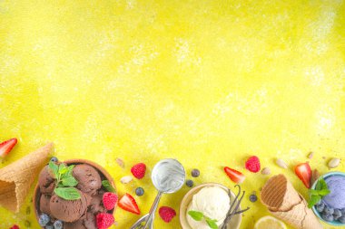 Farklı kaselerde çeşitli renkli dondurma topları, dondurma külahları ve aromalı malzemeler - şam fıstığı, böğürtlen, limon, çikolata, vanilya, nane. Renkli sarı parlak arkaplan