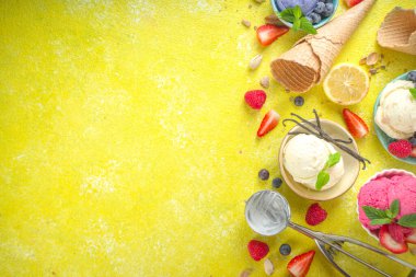 Farklı kaselerde çeşitli renkli dondurma topları, dondurma külahları ve aromalı malzemeler - şam fıstığı, böğürtlen, limon, çikolata, vanilya, nane. Renkli sarı parlak arkaplan