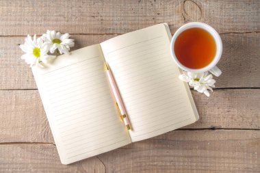 Baharda ya da sonbahar çayının başında papatya çiçekleri ve not defteriyle sıcak bir kahvaltı. Boşluğu kopyala, üst görünüm düzlüğü 