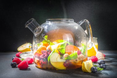 Çaydanlıkta meyve ve çilek çayı. Limonlu, naneli, yabanmersinli, zencefilli, portakallı, elmalı sıcak içecek. Koyu mavi arkaplan fotokopi alanında sıcak aromalı buhar içeceği  