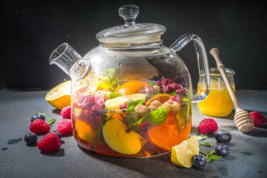 Çaydanlıkta meyve ve çilek çayı. Limonlu, naneli, yabanmersinli, zencefilli, portakallı, elmalı sıcak içecek. Koyu mavi arkaplan fotokopi alanında sıcak aromalı buhar içeceği  