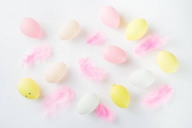 Paskalya yumurtaları ve beyaz masasında tüyleri olan pastel renkli düz yatak. Paskalya şablonu basit arka plan, bahar tatili konsepti 