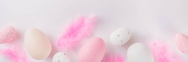 Paskalya yumurtaları ve beyaz masasında tüyleri olan pastel renkli düz yatak. Paskalya şablonu basit arka plan, bahar tatili konsepti 